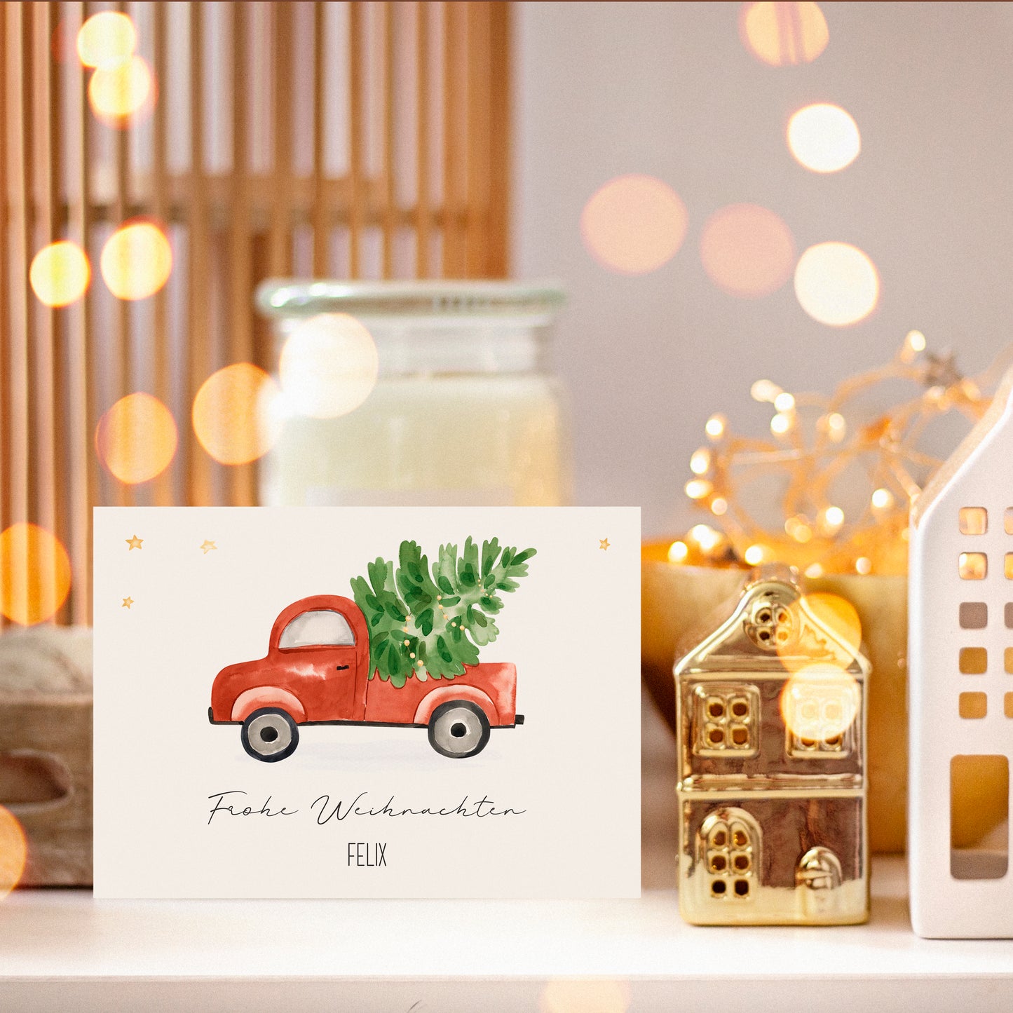 Personalisierte Weihnachtskarte Auto & Baum A6 zeigt einen roten Lastwagen mit Tannenbaum. Begleitet von dekorativen Haus-Ornamenten und Lichterkette für festliche Grüße.