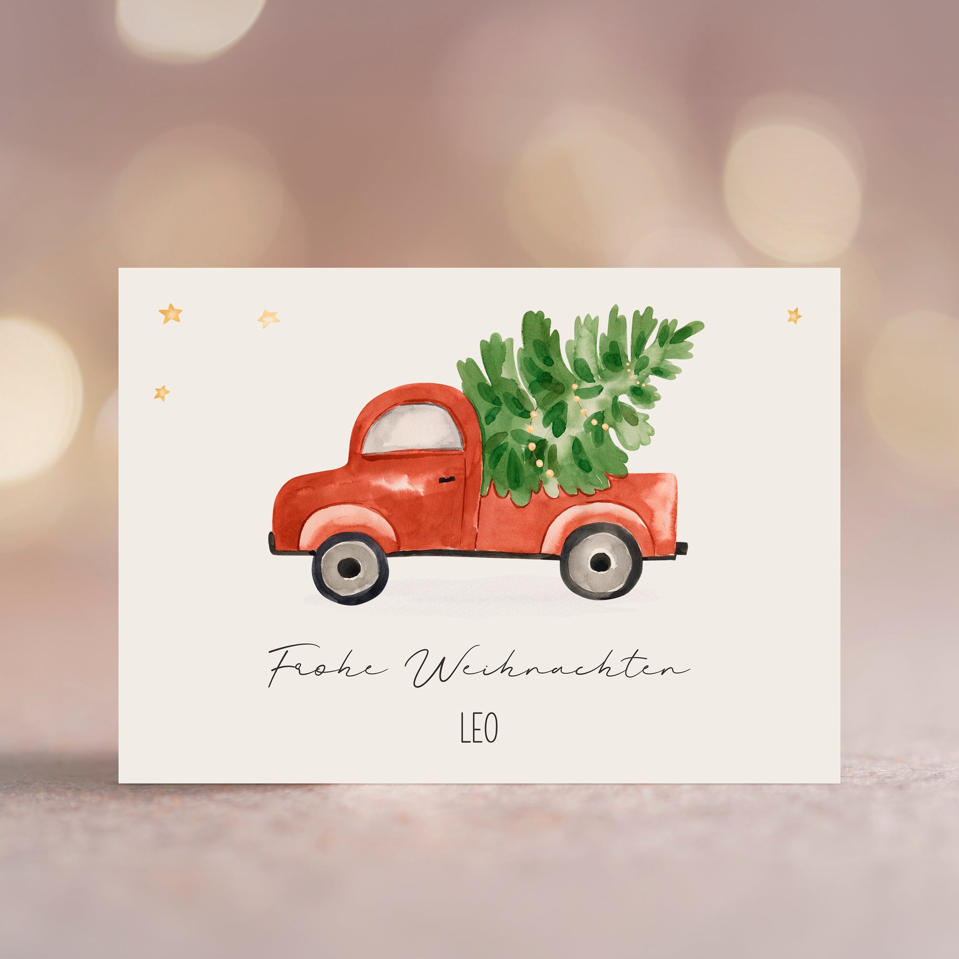 Personalisierte Weihnachtskarte Auto & Baum A6 zeigt einen roten Pickup mit Weihnachtsbaum, umgeben von goldenen Sternen und dem Schriftzug „Frohe Weihnachten“ und „LEO“.