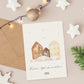Personalisierte Weihnachtskarte Häuser A6 mit winterlichen Aquarellhäusern, umgeben von Dekorationen wie einem Umschlag, Lichterkette und Sternen, ideal für festliche Grüße.