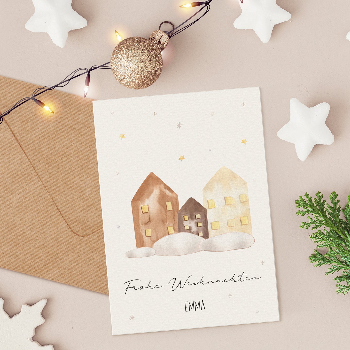 Personalisierte Weihnachtskarte Häuser A6 mit winterlichen Aquarellhäusern, umgeben von Dekorationen wie einem Umschlag, Lichterkette und Sternen, ideal für festliche Grüße.