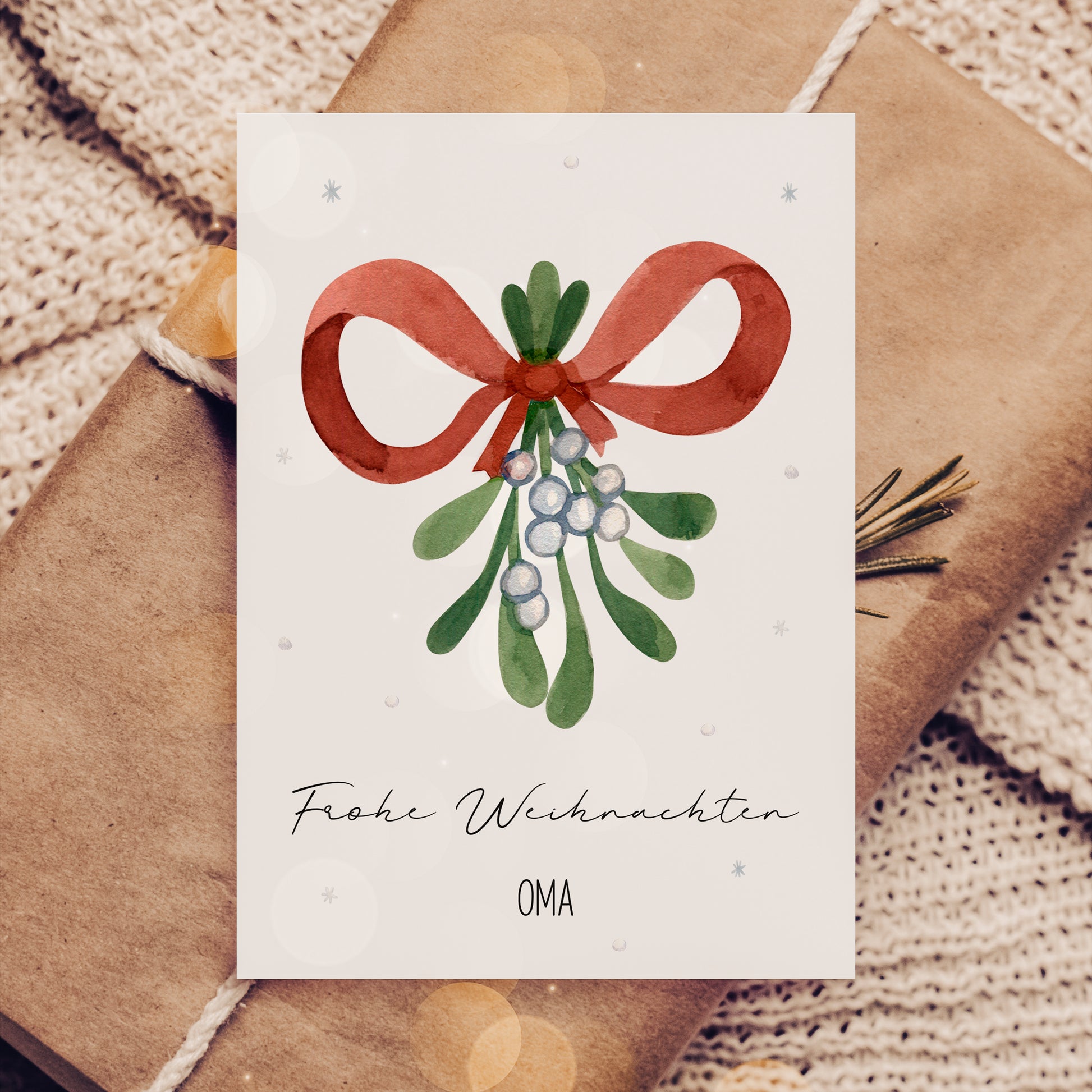 Personalisierte Weihnachtskarte Mistelzweig A6 zeigt Aquarell-Mistelzweig mit roter Schleife und Frohe Weihnachten sowie OMA, auf braun verpacktem Geschenk liegend.