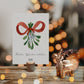 Personalisierte Weihnachtskarte Mistelzweig A6 auf Holztisch, mit handgemaltem Mistelzweig und Frohe Weihnachten in Script. Daneben ein Rentier-Teelichthalter aus Metall.