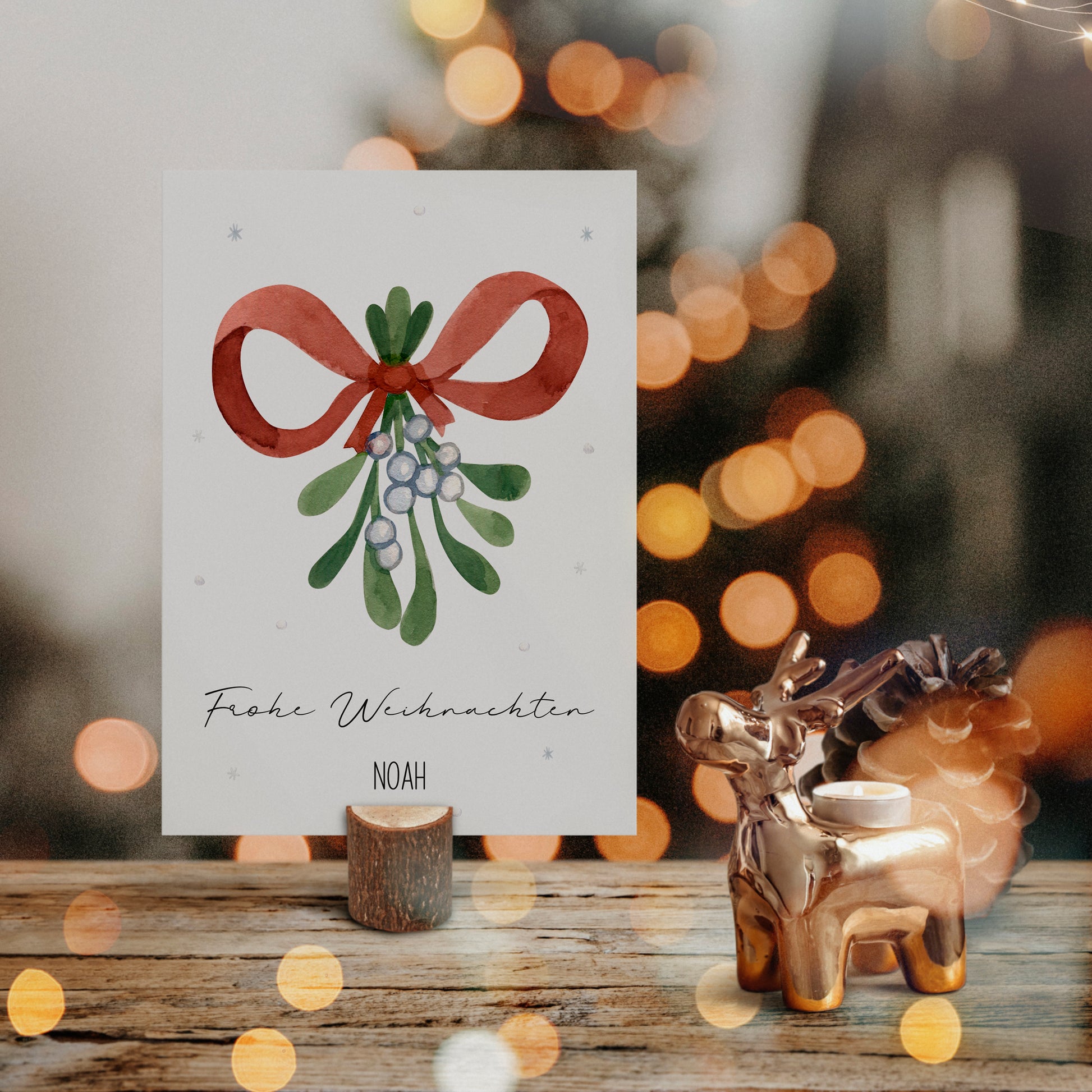 Personalisierte Weihnachtskarte Mistelzweig A6 auf Holztisch, mit handgemaltem Mistelzweig und Frohe Weihnachten in Script. Daneben ein Rentier-Teelichthalter aus Metall.