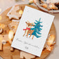 Weihnachtsszene mit Personalisierte Weihnachtskarte Reh & Winterwald A6, zeigt ein Reh mit Tannenbaum, umgeben von Lebkuchen, auf Holzbrett.