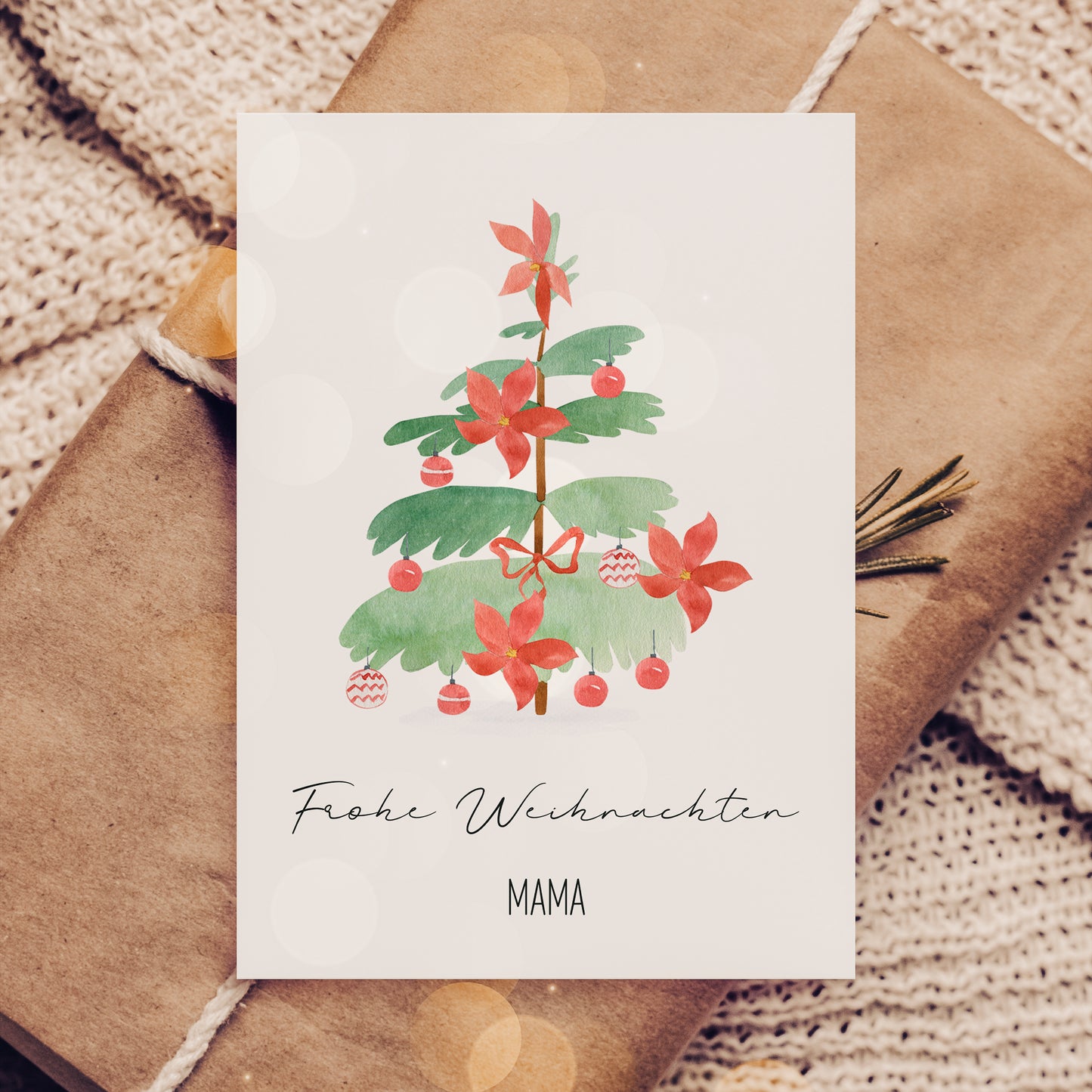 Personalisierte Weihnachtskarte Weihnachtsbaum A6 mit aquarelliertem Tannenbaum, roten Blüten und Kugeln. Beschriftet mit Frohe Weihnachten MAMA, liegend auf Geschenk.