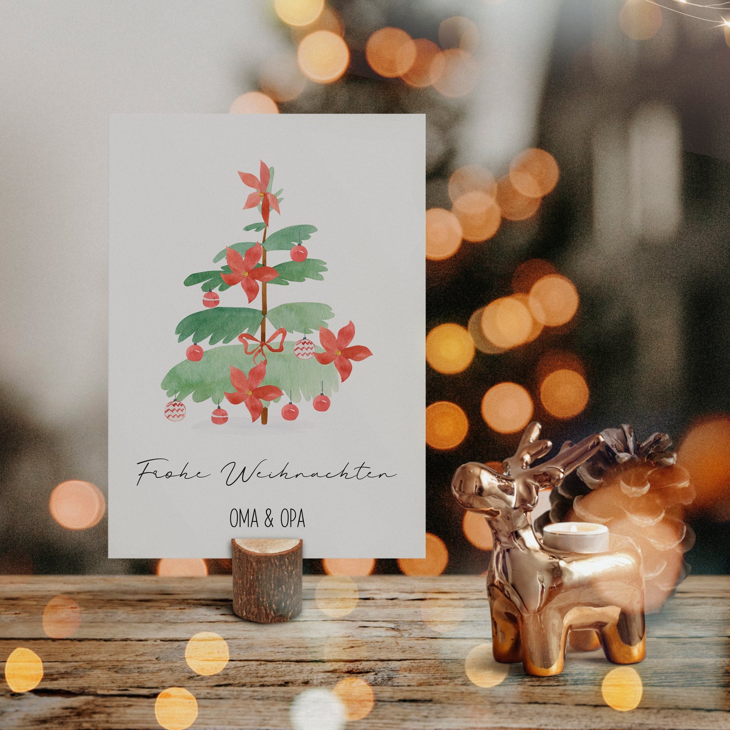 Personalisierte Weihnachtskarte Weihnachtsbaum A6 mit Aquarell-Weihnachtsbaum, Frohe Weihnachten und Namen. Neben goldfarbenem Rentier-Teelichthalter und Tannenzapfen auf Holz.