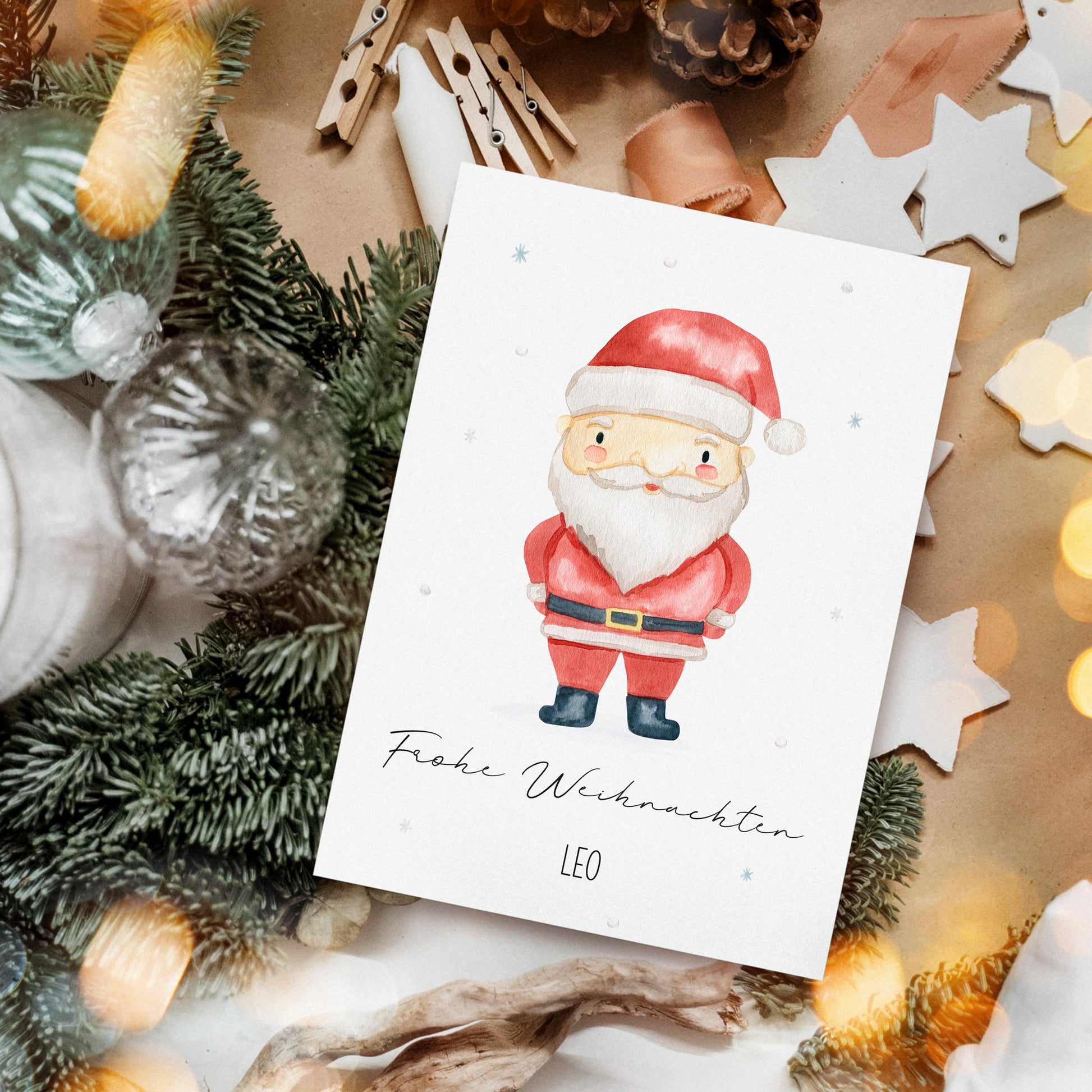 Personalisierte Weihnachtskarte Weihnachtsmann A6 mit Santa-Motiv und Frohe Weihnachten Text, umgeben von Weihnachtsdekorationen wie Tannenzweigen, Holzsternen und Glaskugeln.