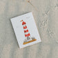 Postkarte Leuchtturm A6 auf Sand, zeigt einen rot-weiß gestreiften Leuchtturm mit Möwen. Gedruckt auf stabilem 300g Naturpapier, ideal für maritime Grüße.