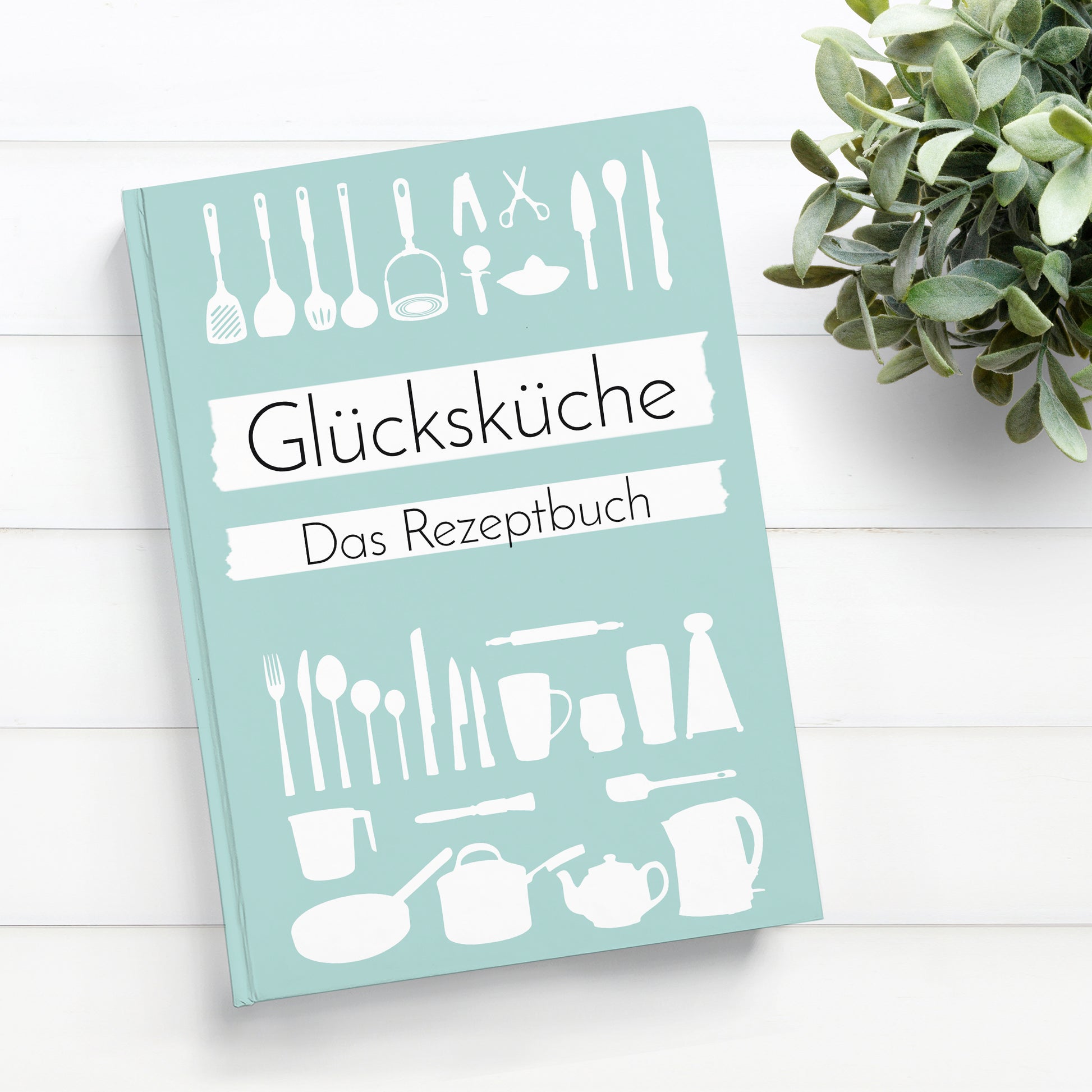 Rezeptbuch zum Selberschreiben A5 Hardcover Glücksküche auf Tisch mit Pflanze, zeigt Inhaltsverzeichnis und Platz für kreative Rezepte. Ideal für persönliche Rezeptsammlungen.