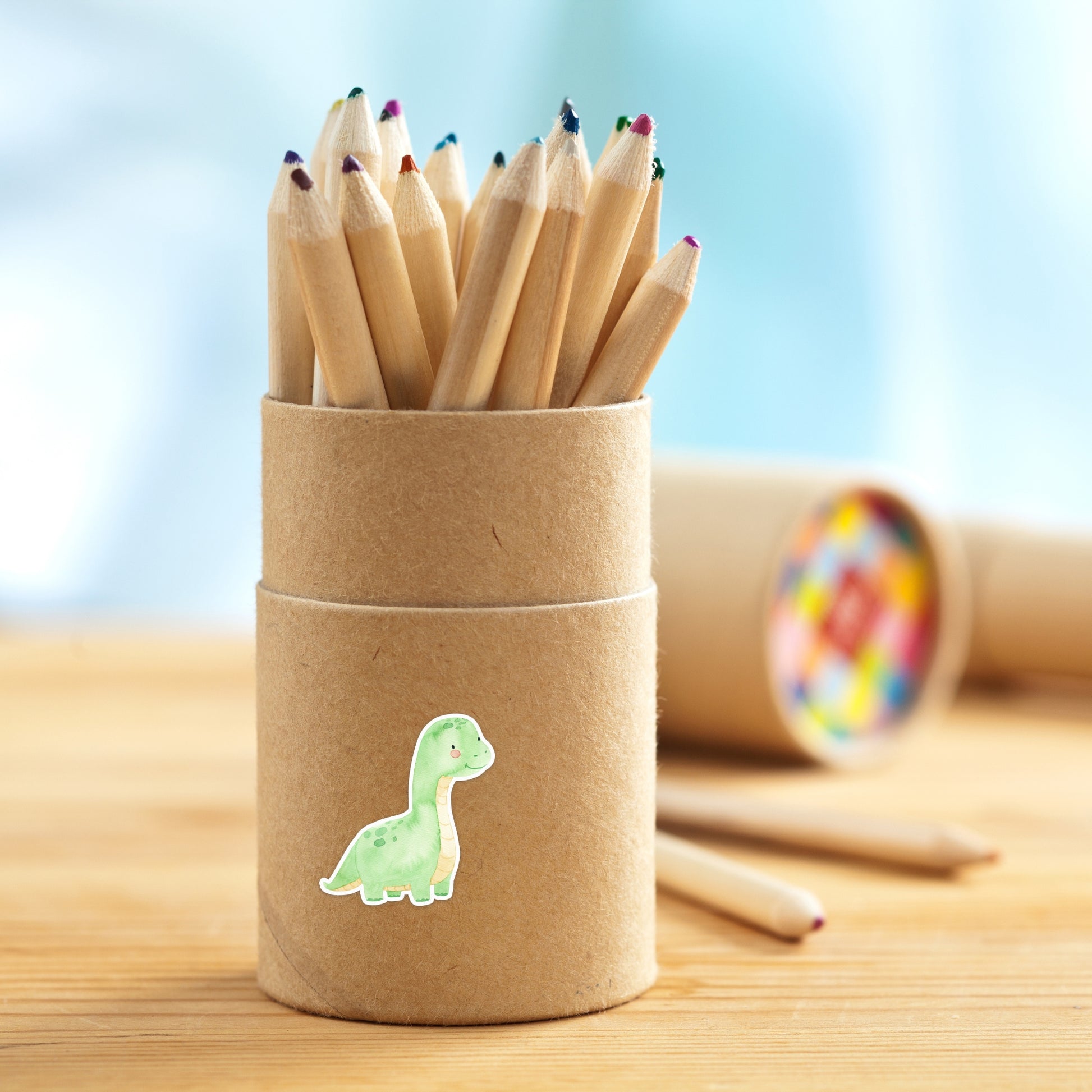 Kleine Kraftpapierrolle mit Sticker Dinosaurier hellgrün, gefüllt mit farbigen Buntstiften. Der handgefertigte, langlebige Aufkleber ist ein spritzgeschützter Blickfang.
