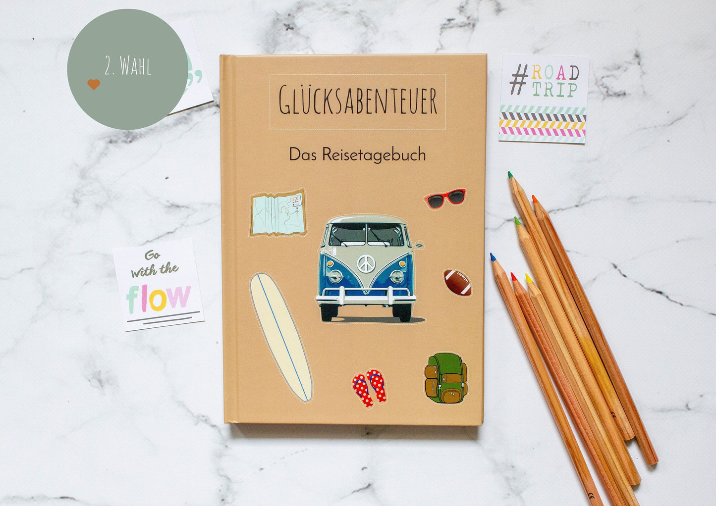 Reisetagebuch A5 Hardcover Vanlife Mängelexemplar mit Van- und Surfbrettzeichnung, inklusive Packlisten und Tagesseiten zum Ausfüllen, auf Marmoroberfläche mit Bleistiften abgebildet.