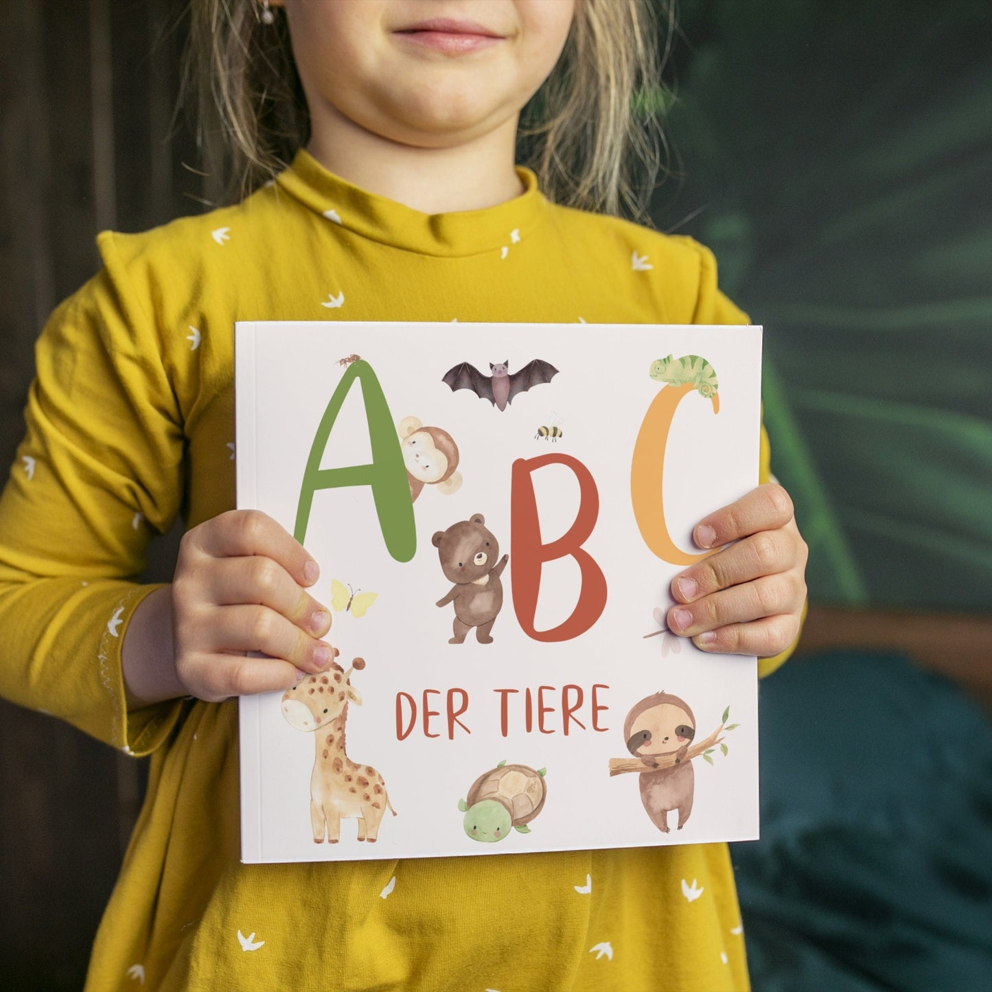 Ein Mädchen hält das Alphabet Buch - ABC der Tiere mit niedlichen Tierillustrationen und Buchstaben in den Händen.