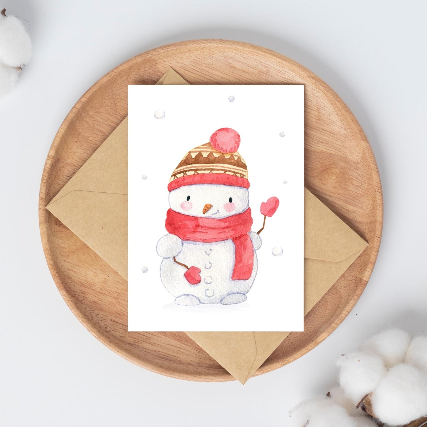 Weihnachtskarte Schneemann rot A6: Eine Weihnachtskarte mit einer süßen Illustration eines Schneemanns, auf einem Holzteller platziert, ohne zusätzliche Dekoration.