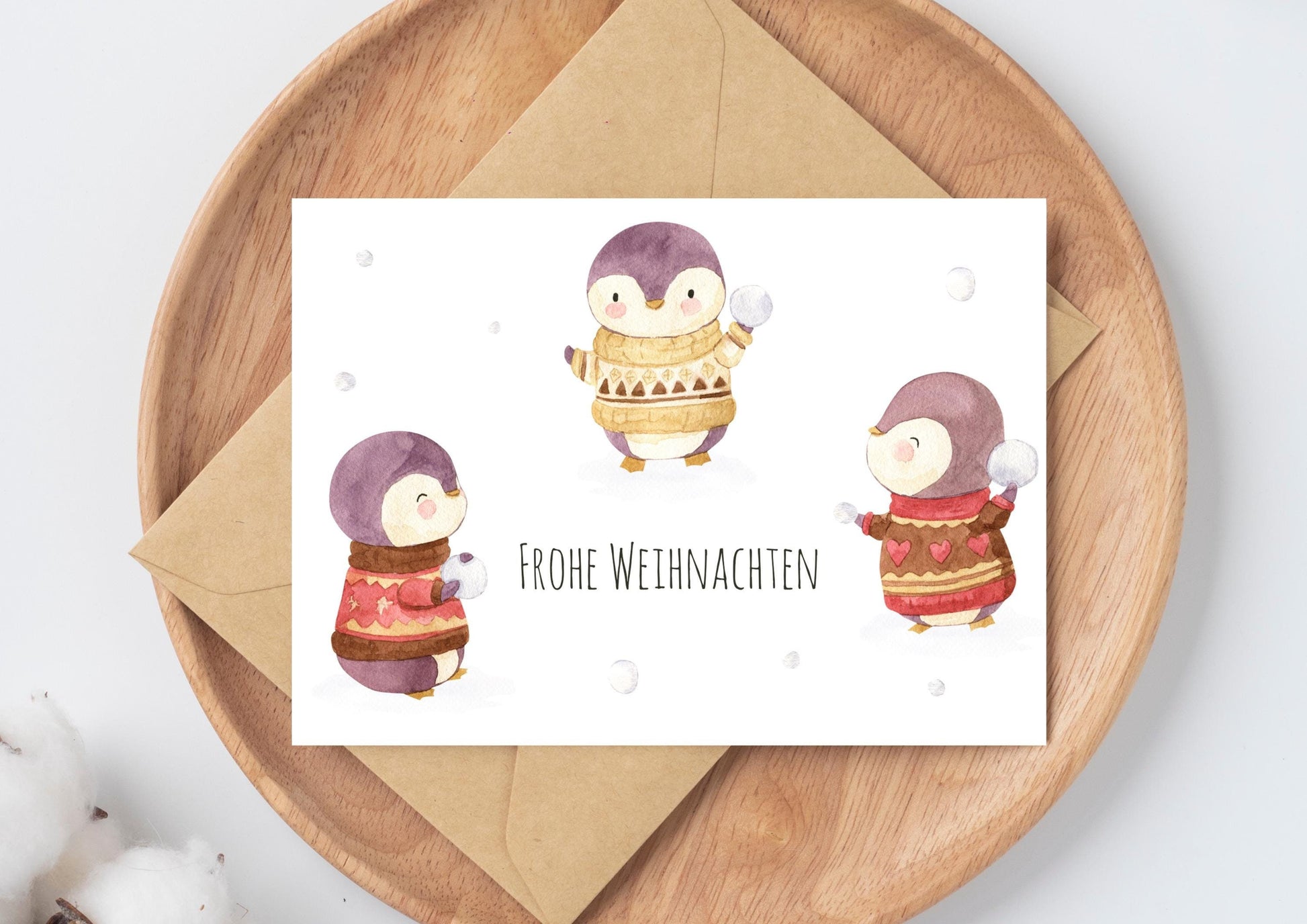 Weihnachtskarte Schneeballschlacht Frohe Weihnachten A6 mit süßer Illustration: Pinguine in Pullovern. Beiliegend ein passender Umschlag auf einem Holztablett.