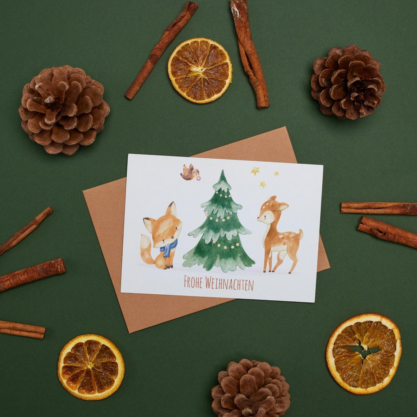 Weihnachtskarte Reh & Fuchs Frohe Weihnachten A6 mit Tieren und Weihnachtsbaum, umgeben von Tannenzapfen und Orangenscheiben.