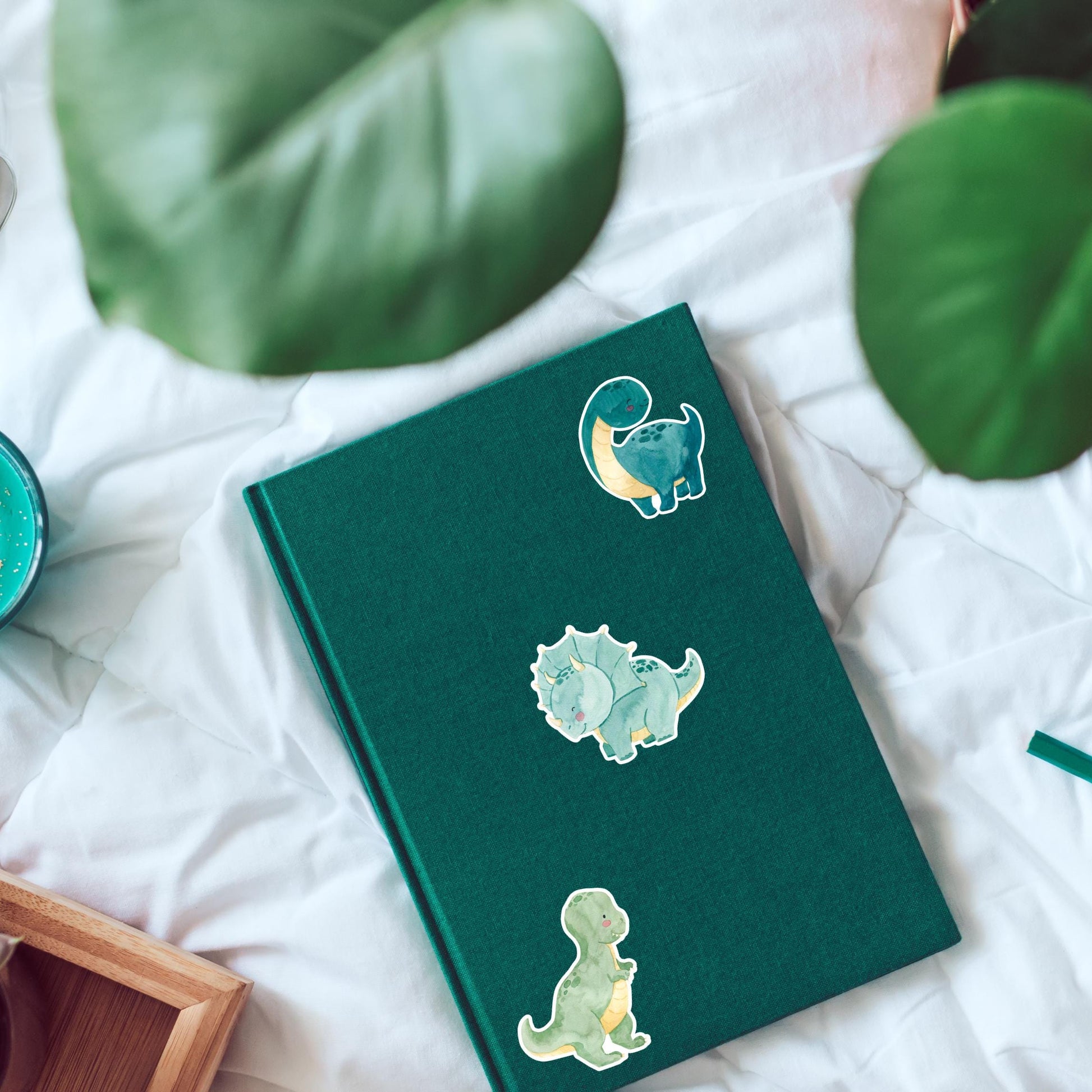 Sticker Dinosaurier dunkelgrün auf grünem Buch mit Cartoon-Dinosaurier. Hochwertiger Vinyl-Sticker, ideal für Bullet Journals oder Laptops. Perfekt für Dino-Fans.