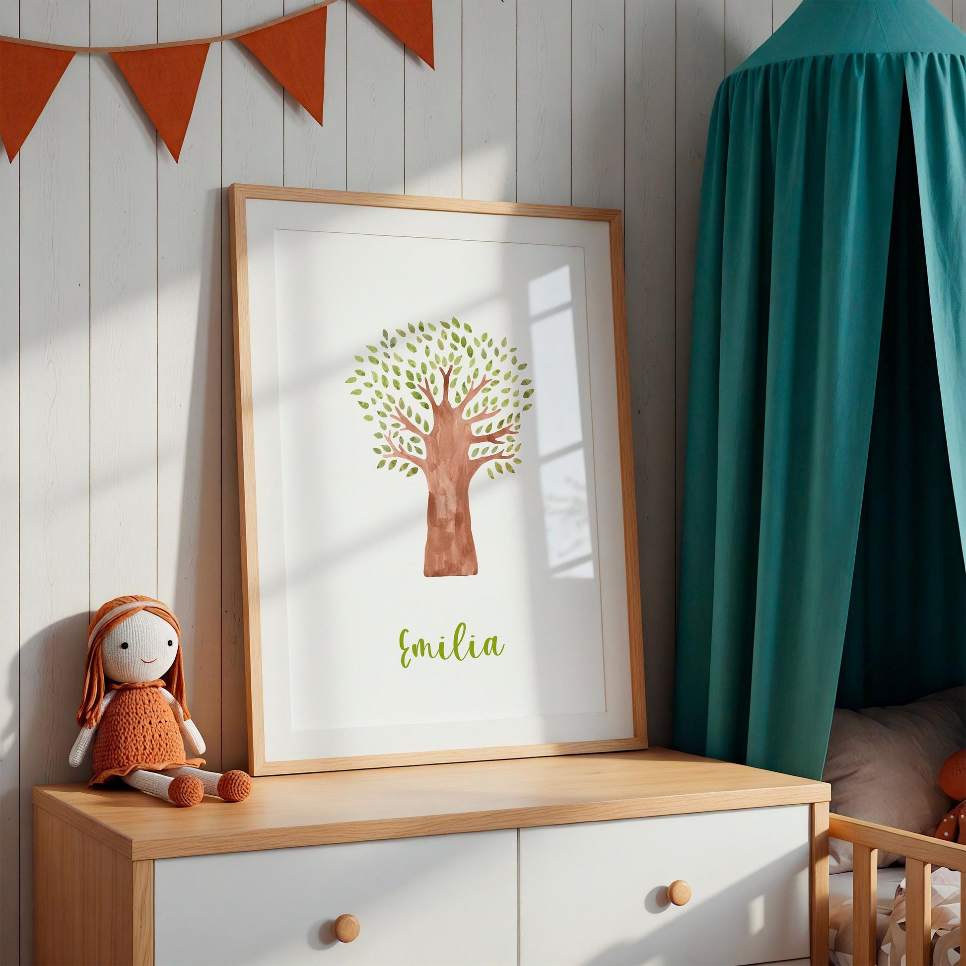 Geburtsposter Baum personalisiert: Holzrahmen mit Aquarellbaum und Emilia darauf, auf heller Kommode, daneben handgestrickte Puppe, orange Wimpelkette darüber.
