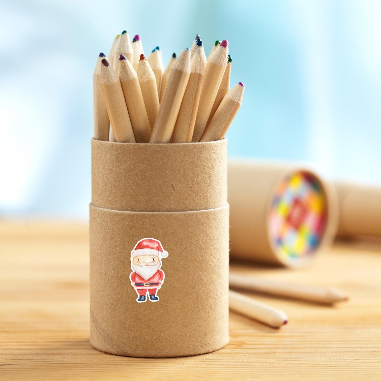 Kraft-Papier-Röhre mit kurzen Holzstiften, verziert mit einem Sticker Weihnachtsmann. Ideal für kreative Weihnachtsprojekte und Geschenkverzierungen.