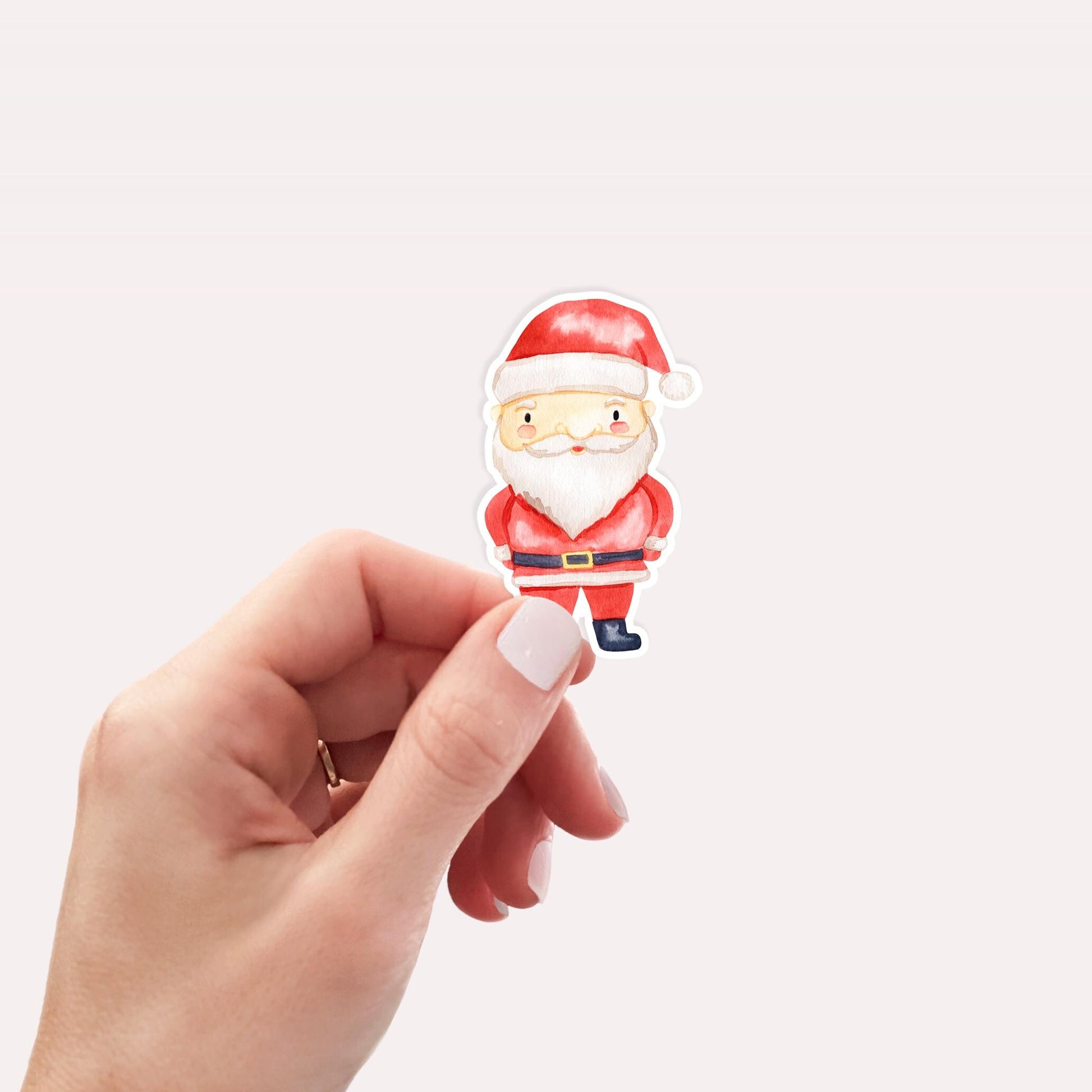 Sticker Weihnachtsmann: Hand hält kleinen Sticker von Santa Claus im klassischen Anzug aus hochwertigem Vinyl, ideal für kreative Weihnachtsdekorationen. 