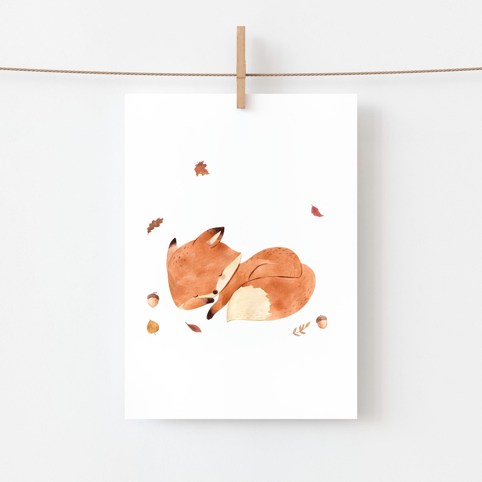 Karte Fuchs & Herbstlaub A6: Illustration eines schlafenden Fuchses umgeben von Herbstlaub, aufgehängt mit einer Holzklammer an einem Seil. Gedruckt auf stabilem Naturpapier.