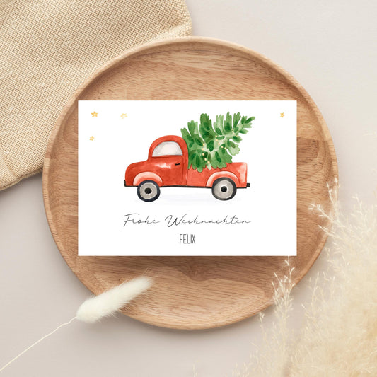 Personalisierte Weihnachtskarte Auto & Baum A6 auf Holzteller, mit vintage rotem Pickup und Weihnachtsbaum, umgeben von natürlichen Elementen, wie Gräsern und Stoff.