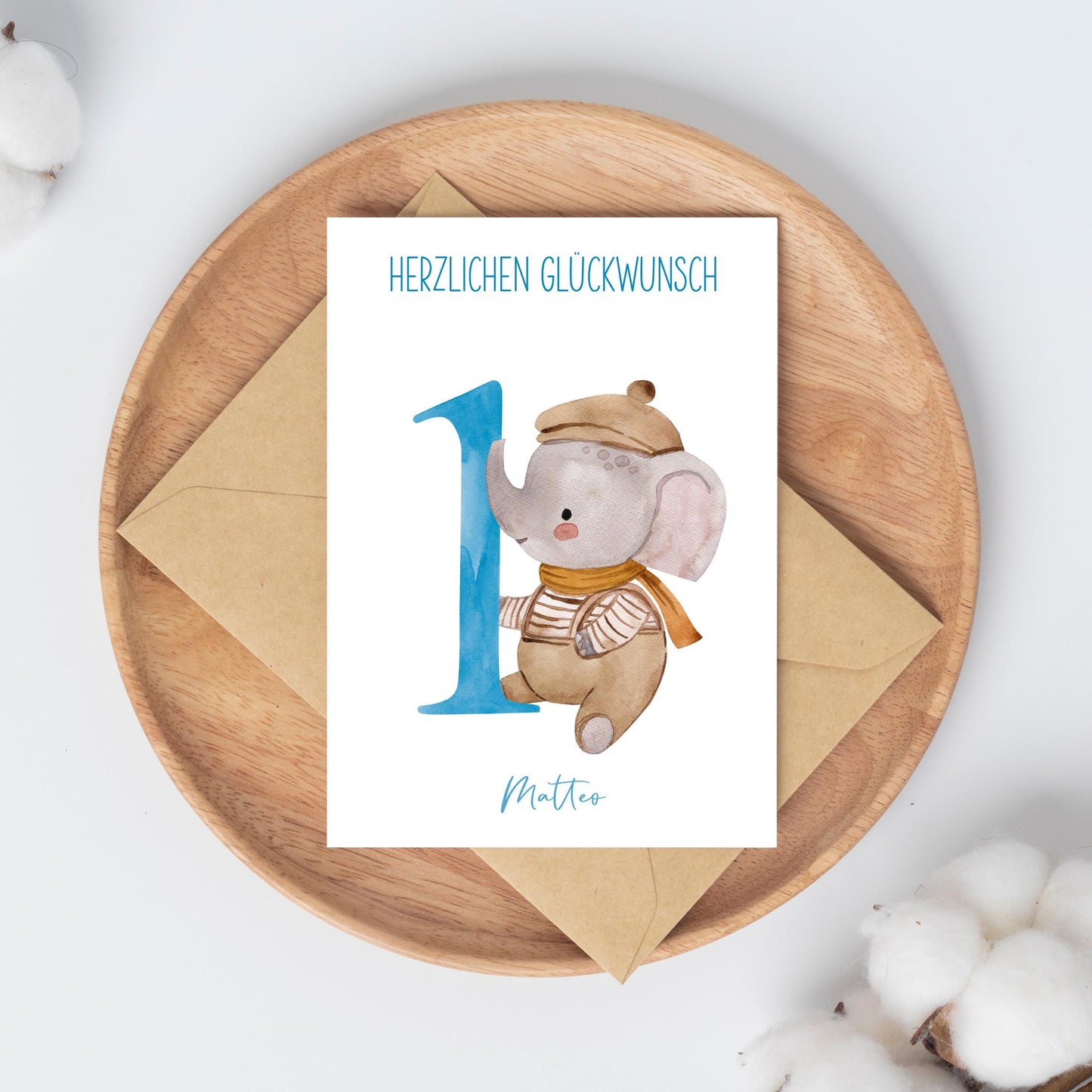 Personalisierte Geburtstagskarte Elefant A6 auf Holzplatte mit Umschlag, verziert mit Baumwollzweigen. Karte zeigt Elefant und Herzlichen Glückwunsch neben Name Matteo.