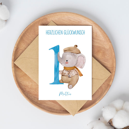 Personalisierte Geburtstagskarte Elefant A6 auf Holzplatte mit Umschlag, verziert mit Baumwollzweigen. Karte zeigt Elefant und Herzlichen Glückwunsch neben Name Matteo.