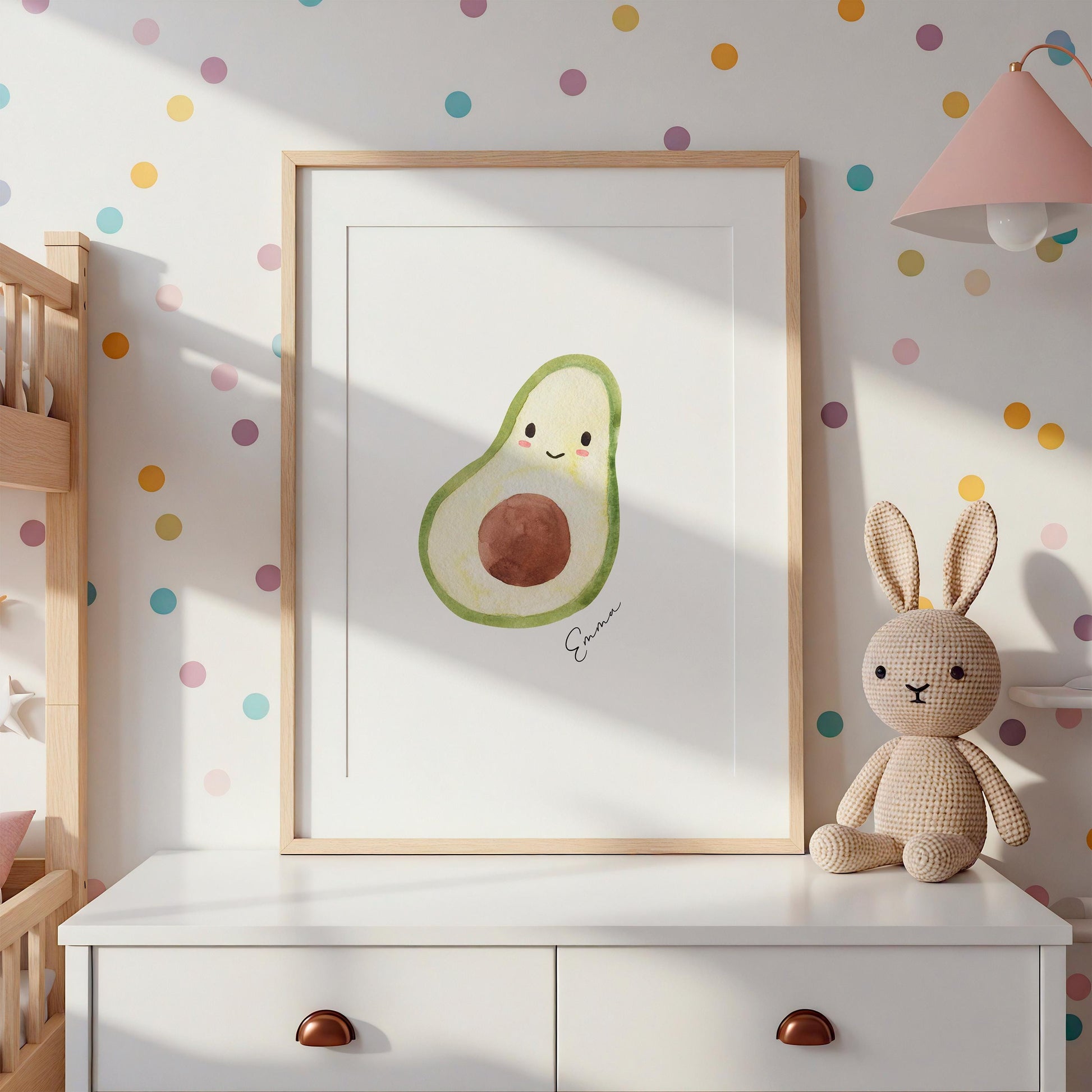 Namensposter Avocado A3 & A4 in hellem Rahmen auf weißer Kommode, daneben neutrale gestrickte Hasenpuppe, pastellfarbene Wandaufkleber im Hintergrund.