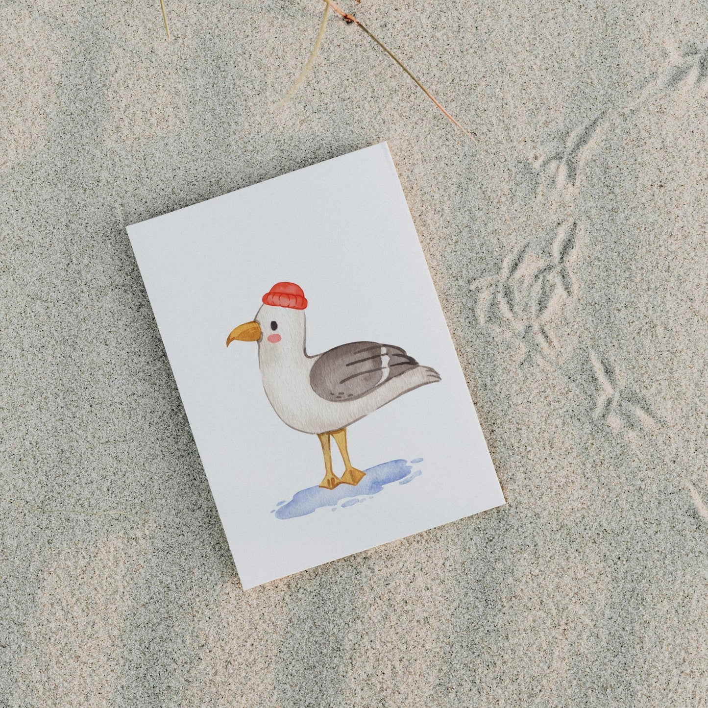 Postkarten Set Meer: Illustration einer Möwe mit roter Mütze auf weißem Papier, liegend im Sand. Teil eines 3er Sets mit maritimen Motiven.