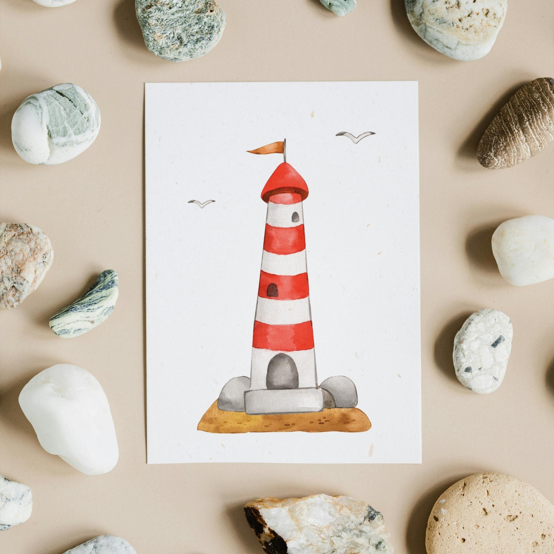 Postkarten Set Meer: 3er Set mit Leuchtturm, Möwe und Segelboot A6, zeigt handgemaltes Leuchtturm-Motiv auf quadratischem Papier, umgeben von Strandkieseln.